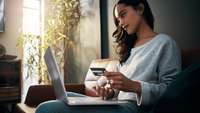 Junge Frau sitzt am Laptop mit einer Kreditkarte in der Hand