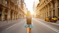 junge Frau mit Rucksack geht auf einer Stadtstraße Richtung Sonnenaufgang