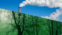 Fabrikschlote vor blauem Himmel, im Vordergrund eine grüne Absperrung