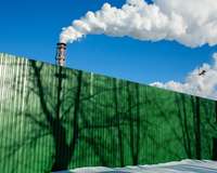 Fabrikschlote vor blauem Himmel, im Vordergrund eine grüne Absperrung