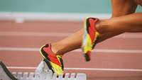 Beine einer Läuferin, die aus dem Startblock sprintet, schwarz-rot-goldene Laufschuhe
