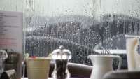 Blick aus einem Fenster in den Regen, im Vordergrund ein gedeckter Tisch