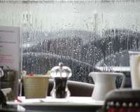 Blick aus einem Fenster in den Regen, im Vordergrund ein gedeckter Tisch