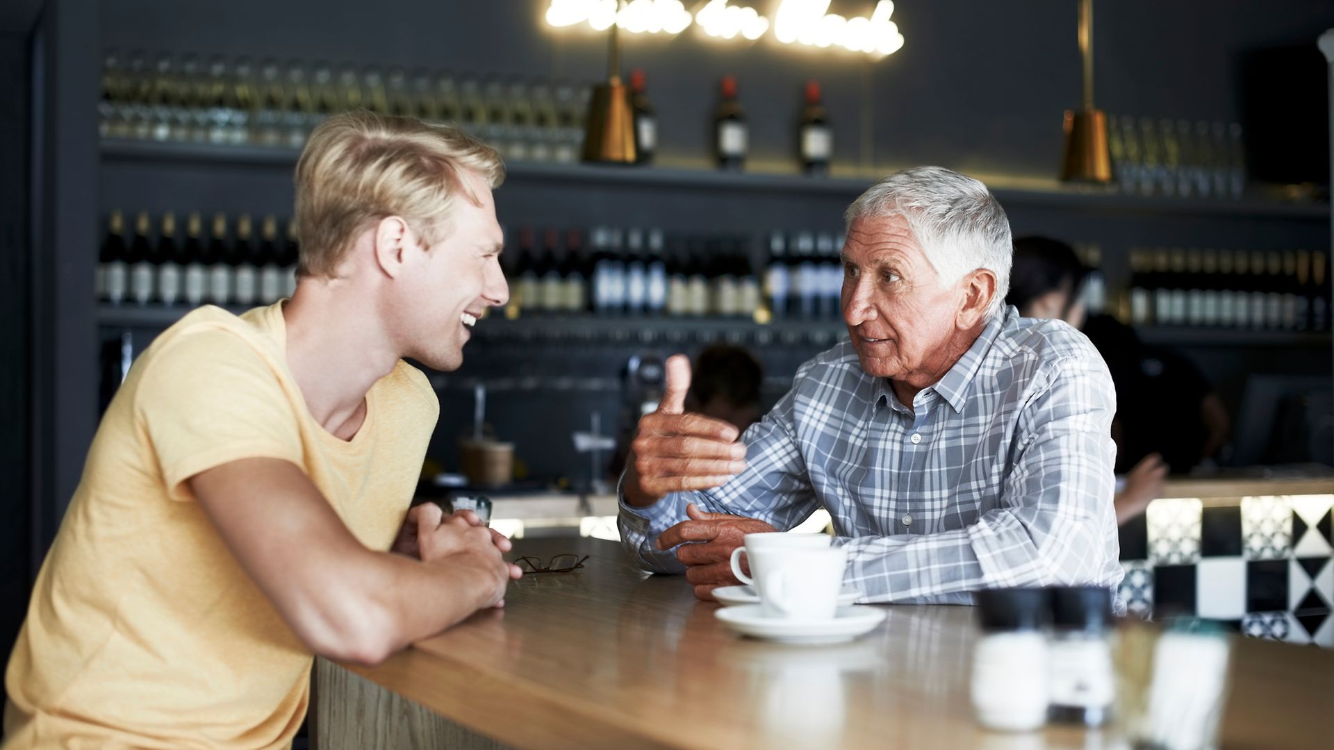 Junger und alter Mann sitzen an einer Theke und trinken Kaffee