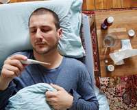 Kranker Mann mit Fieberthermometer und Taschentüchern im Bett