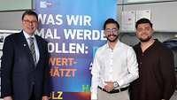 Drei Männer vor einem Plakat