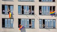 Menschen schauen aus Fenstern und zeigen die bunte LGBTQI+-Fahne