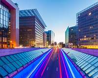 Leere Straße mit Leuchtspuren in Brüssel im Abendlicht, links das Europagebäude